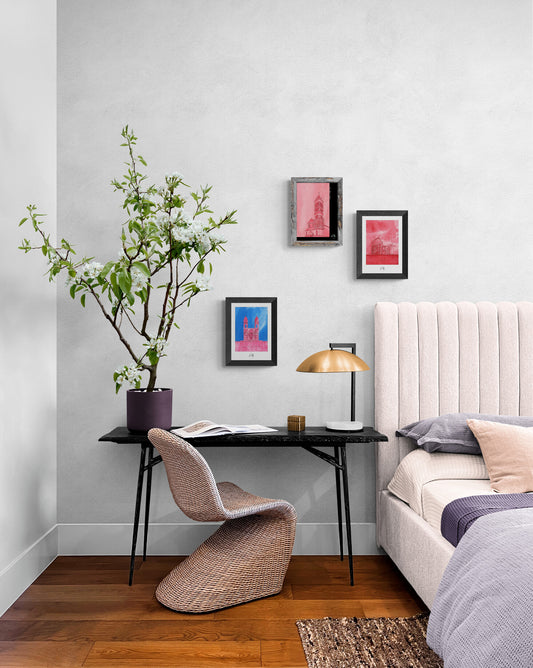 Trois affiches picturales colorées de monuments romains au-dessus d'un bureau avec chaise en rotin dans une chambre